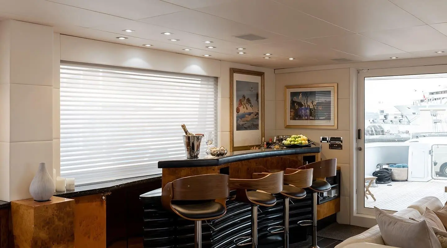 Interior yacht lounge with bar, wooden seating, framed pictures, and window blinds