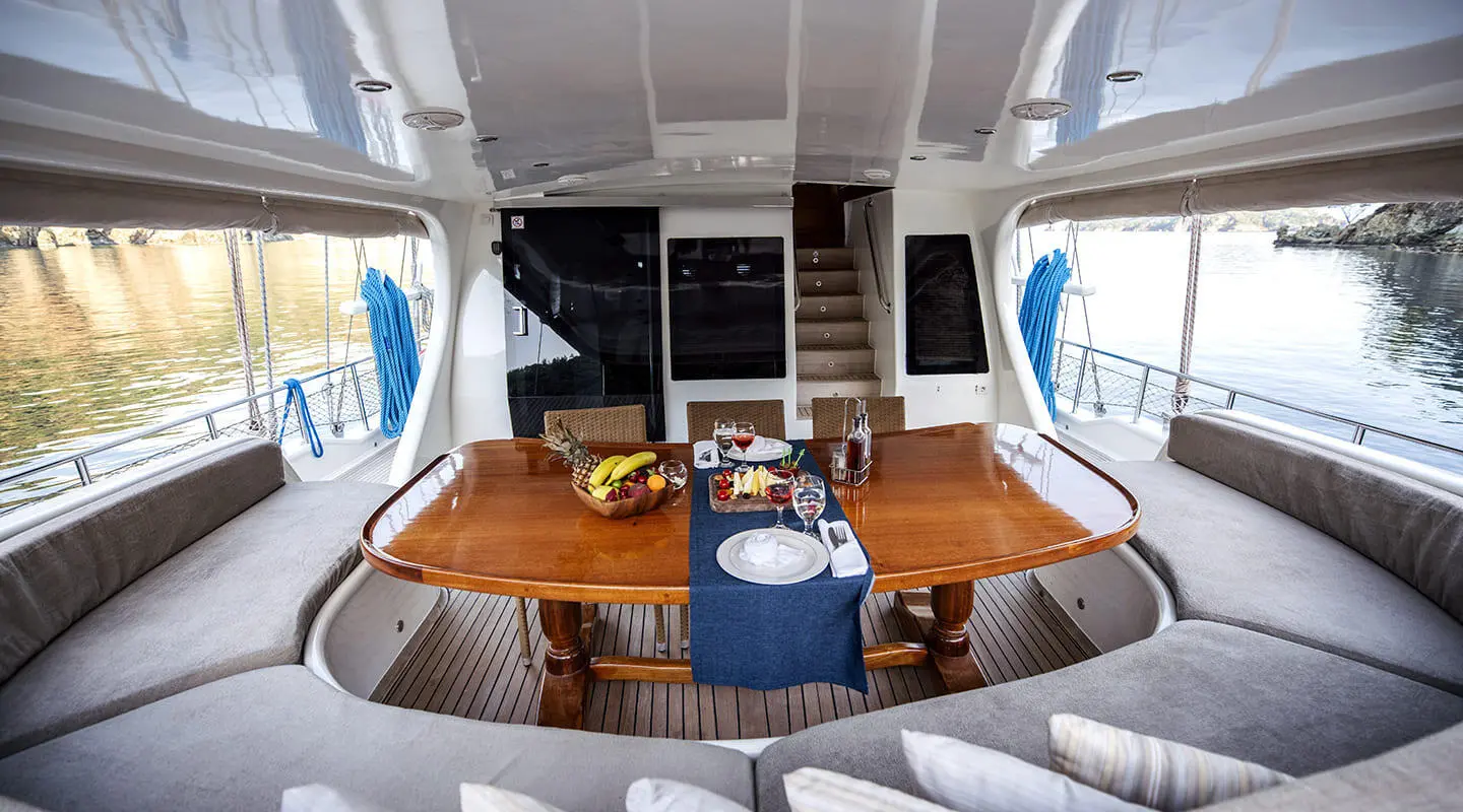 Kayhan 4 yacht helm cockpit with wooden table, cushioned seating, and dining setup at sunset
