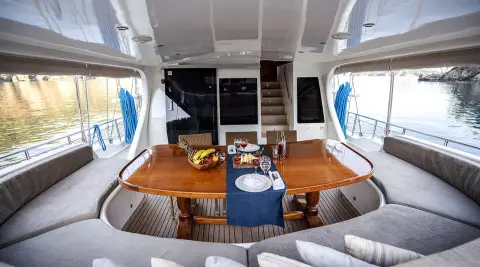 Kayhan 4 yacht helm cockpit with wooden table, cushioned seating, and dining setup at sunset