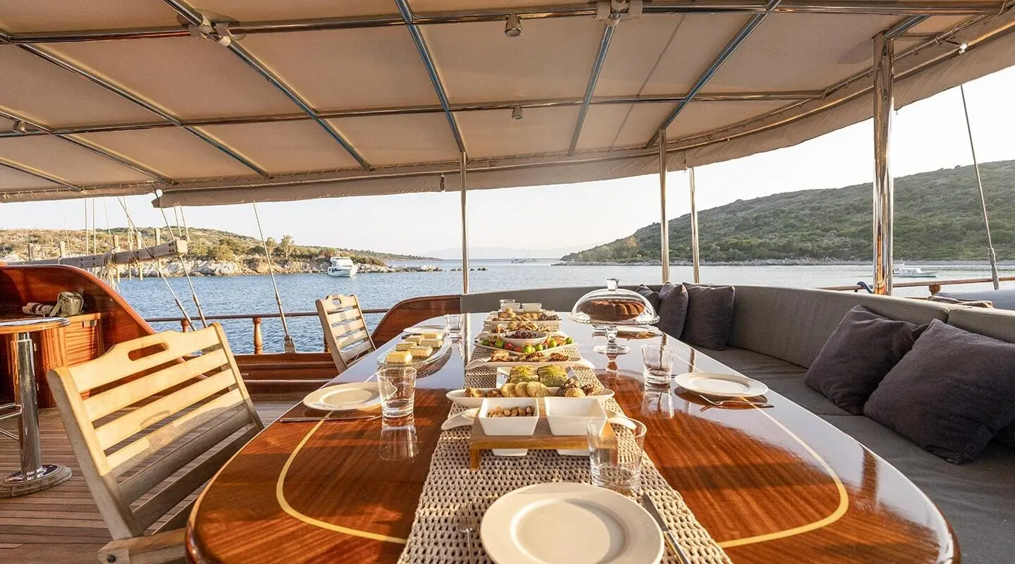 Yacht Bedia Sultan deck at sunset with dining table and cushioned seating on sunlit wood