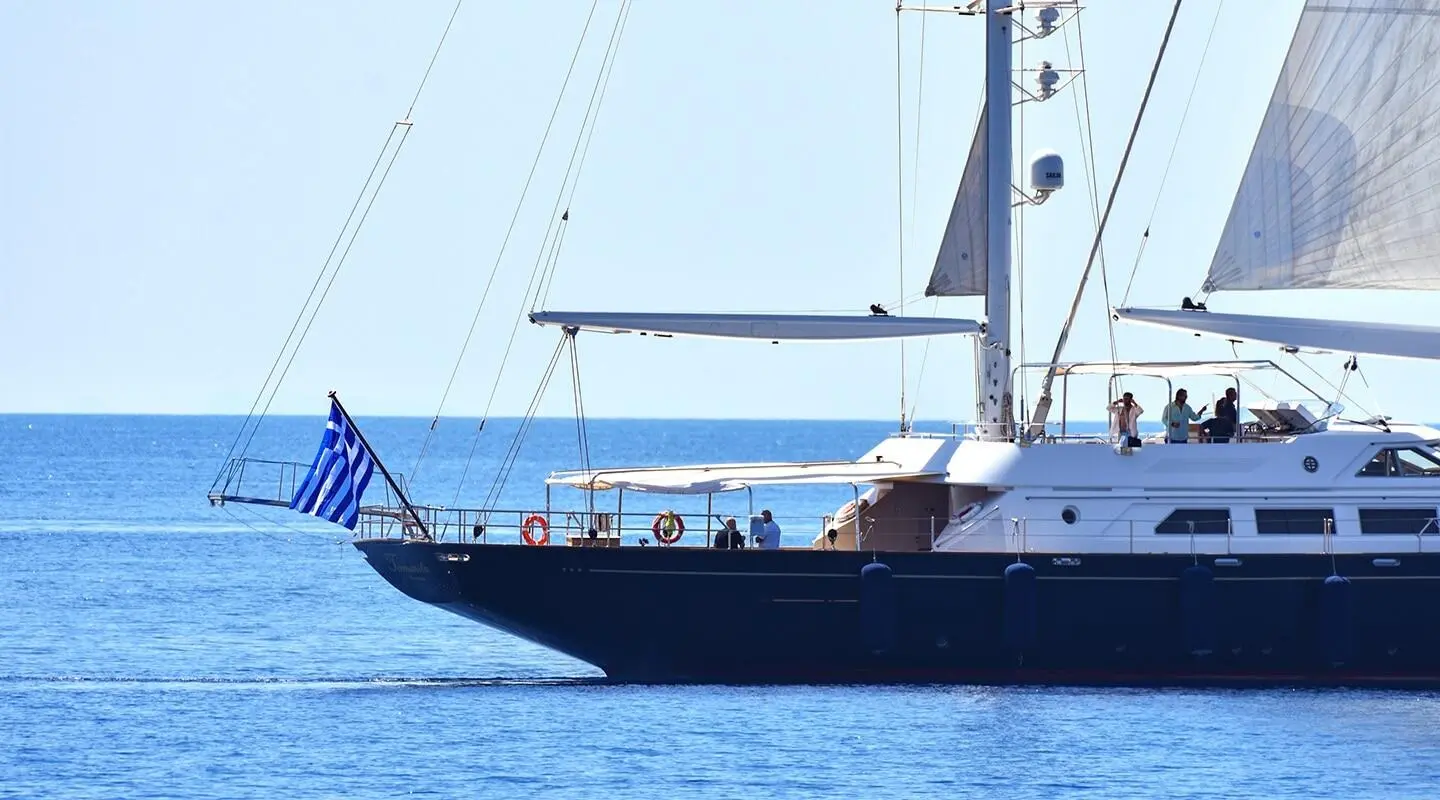 A luxury sailing yacht Tamarita anchored on calm blue water with sails up