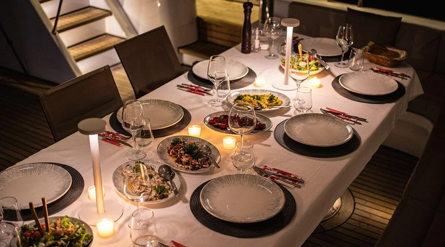 Angelo III yacht charter dining setup on deck at dusk with tableware and candles