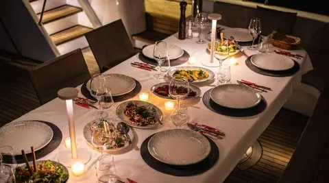 Angelo III yacht charter dining setup on deck at dusk with tableware and candles