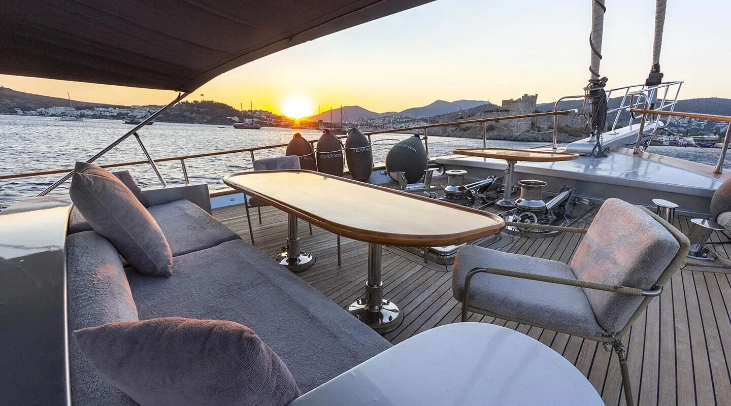 Sunset on a luxury yacht deck with seating, tables, and a calm harbor view