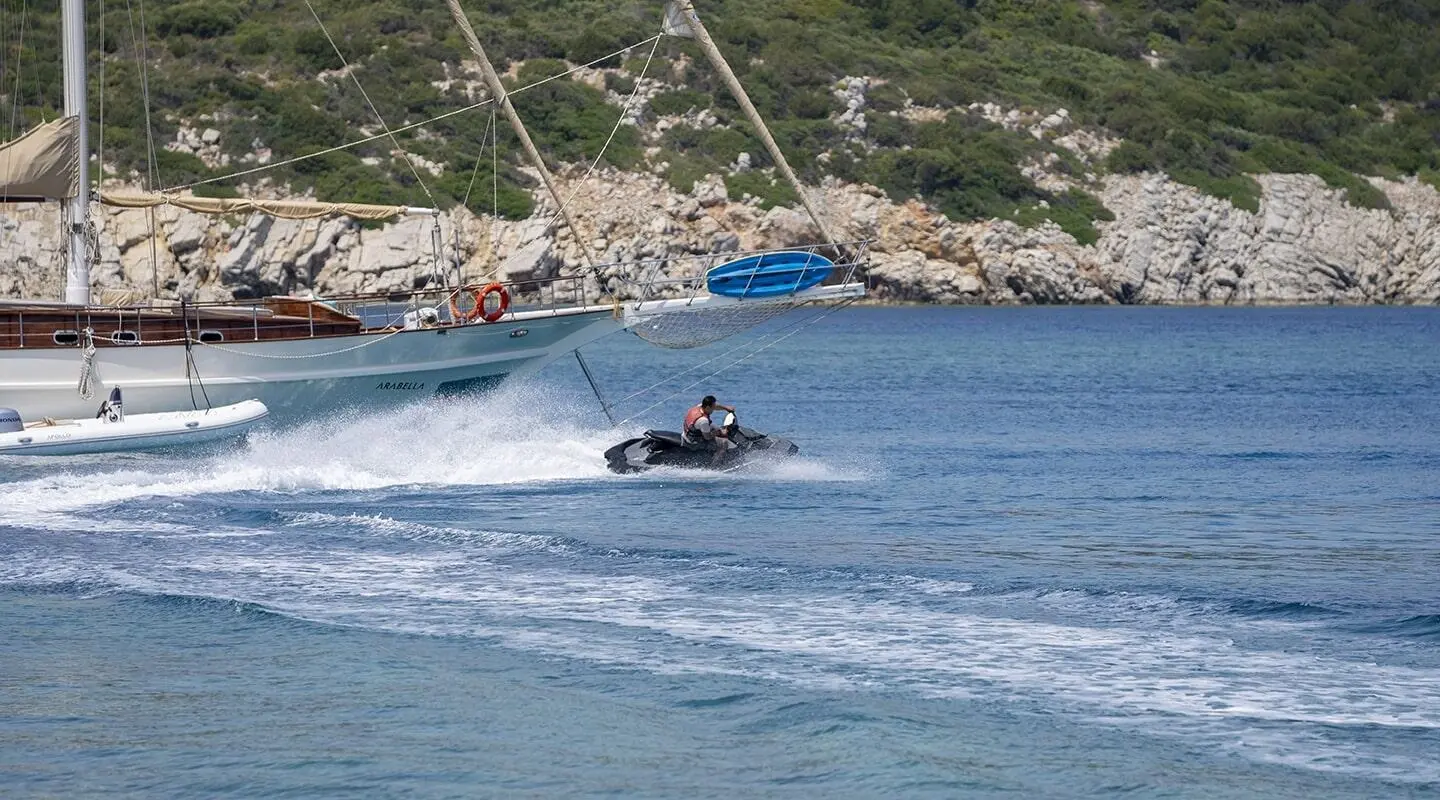 Gulet Arabella yacht at sea with blue water and rocky shoreline nearby
