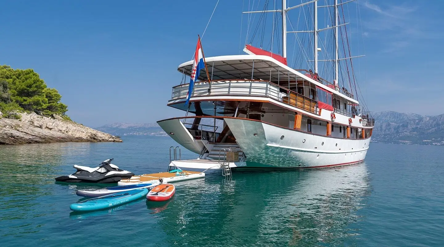 Yacht Barbara docked with gangway and small boat nearby on calm blue water