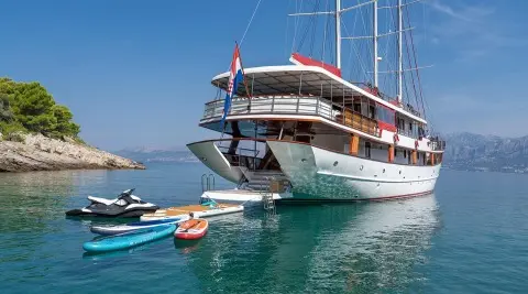 Yacht Barbara docked with gangway and small boat nearby on calm blue water