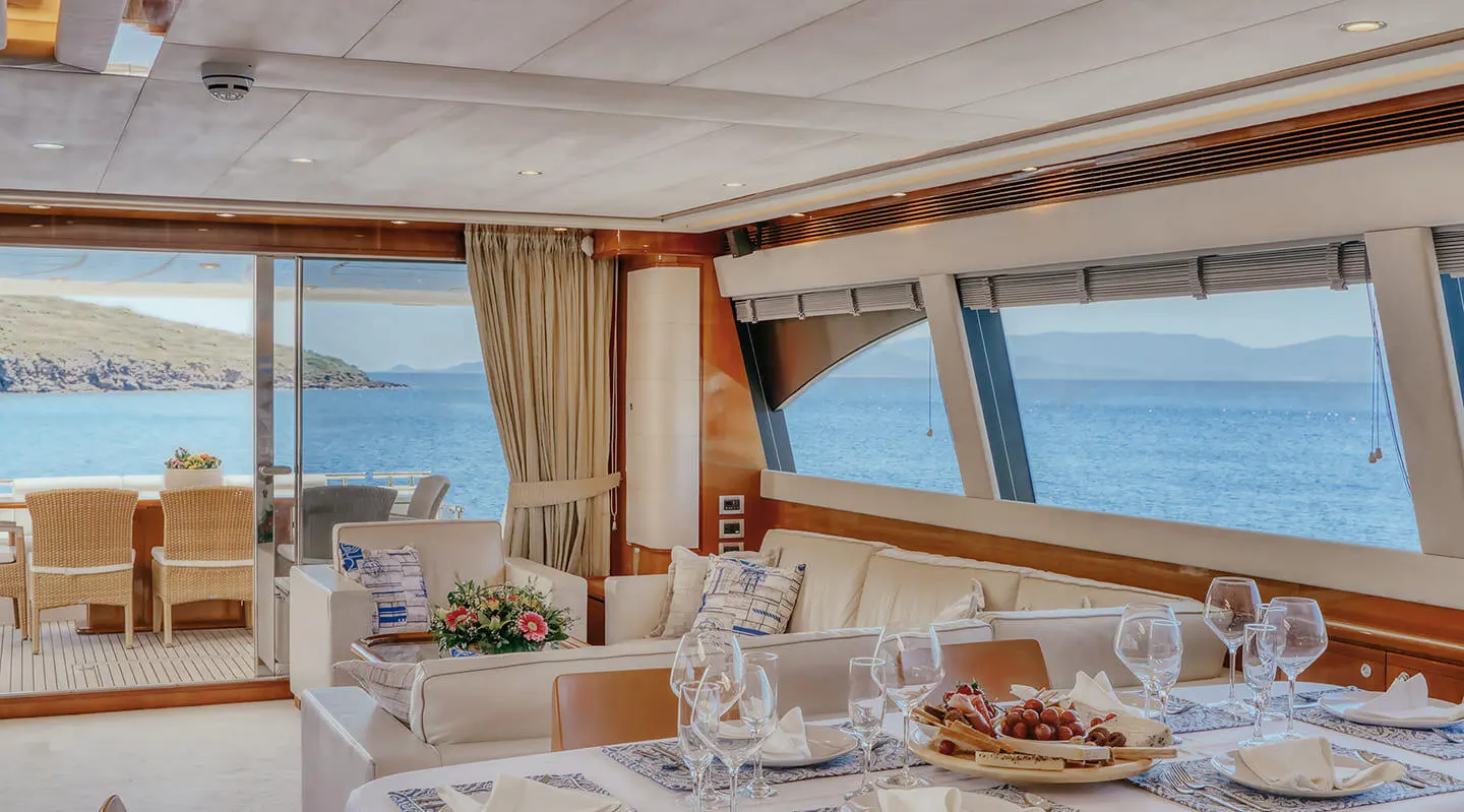Lidia yacht saloon with large windows, beige seating, and table set for dining