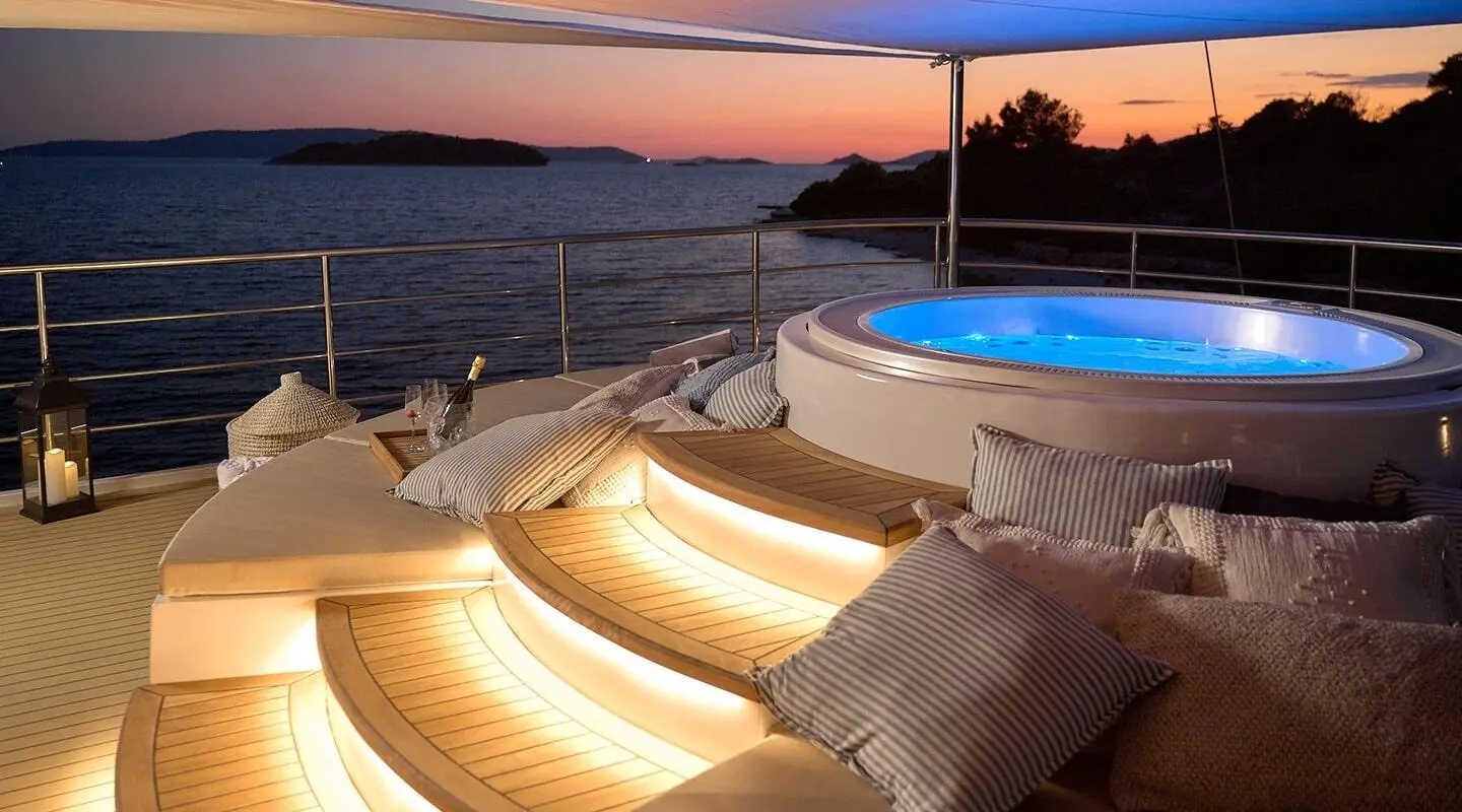 Bellezza on deck at sunset with illuminated curved steps and blue-lit jacuzzi aboard yacht