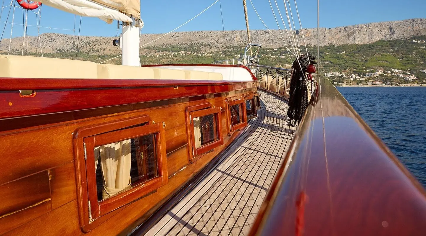 Linda yacht deck with wooden railing, sunset glow, sails in distance, calm water
