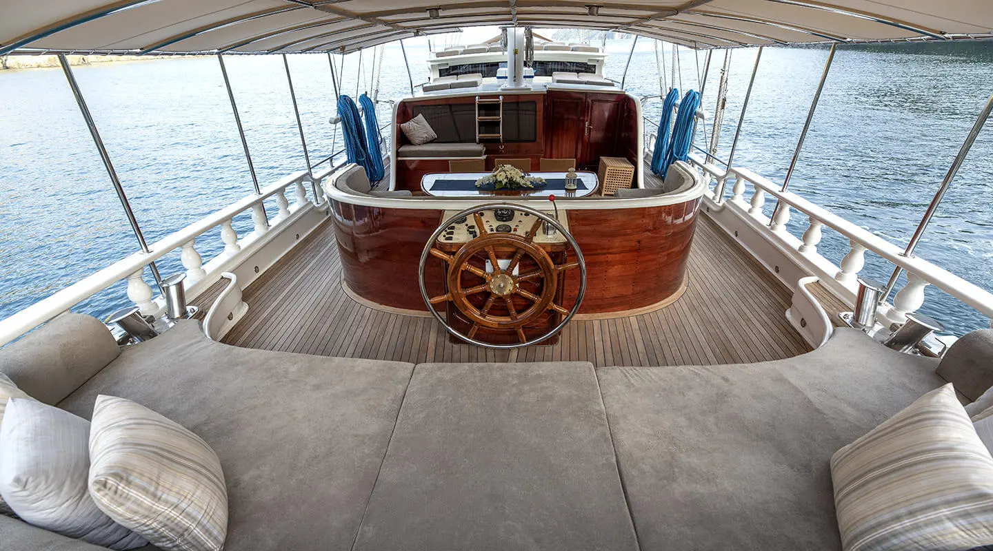 Aft deck of Kayhan 5 gulet with wooden helm and steering wheel, covered seating