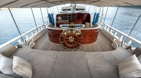 Aft deck of Kayhan 5 gulet with wooden helm and steering wheel, covered seating
