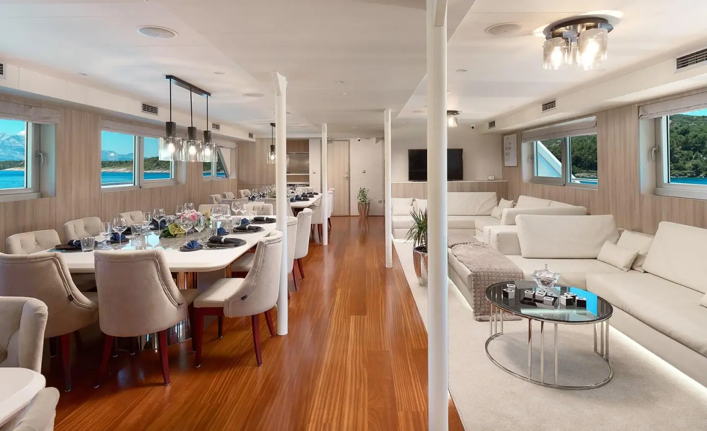 Elegant yacht salon and dining area with white upholstery and wooden floors