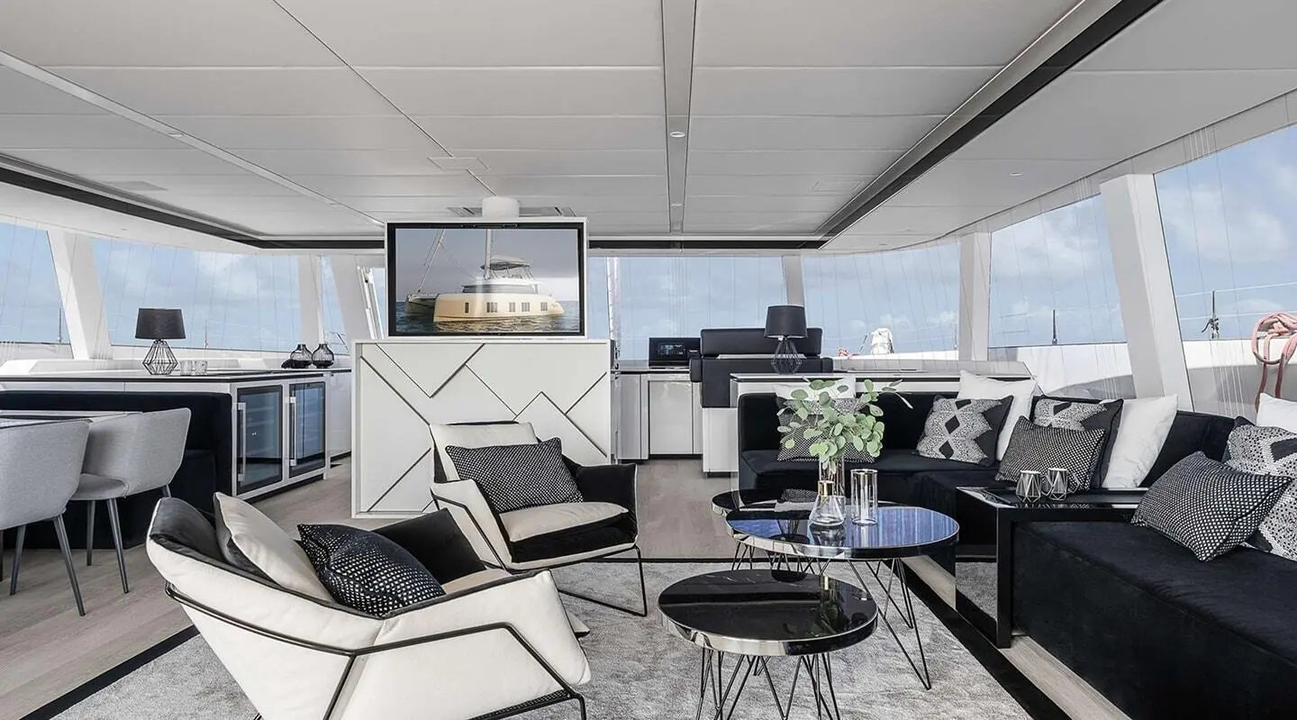 Elegant yacht interior with white seating, glass tables, and large windows at sunset