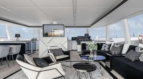 Elegant yacht interior with white seating, glass tables, and large windows at sunset