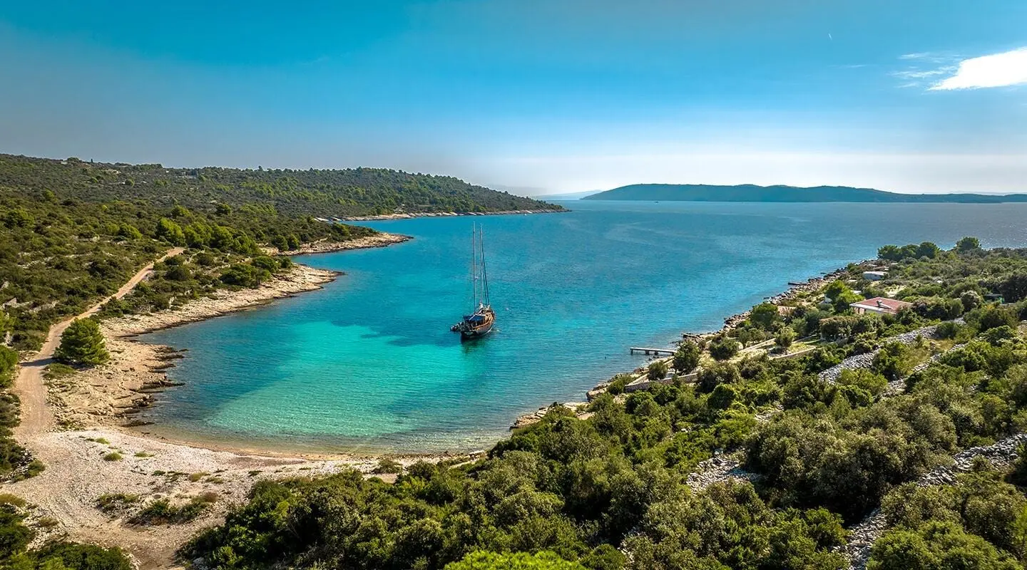 Smart Spirit yacht anchored near a rocky coastline with turquoise sea and clear sky