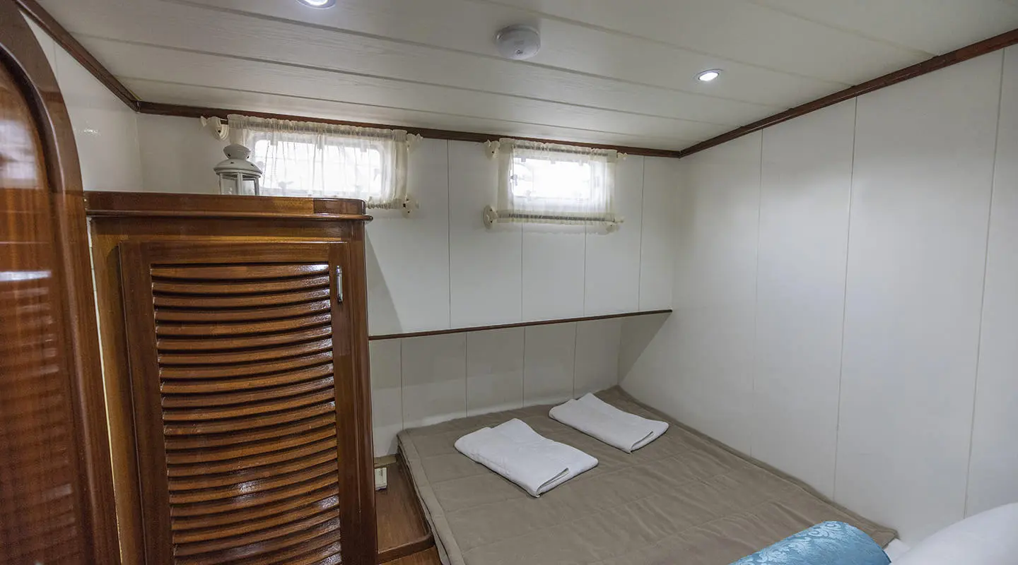 Interior of a yacht cabin with double bed, white walls, wooden slats, and a small window.