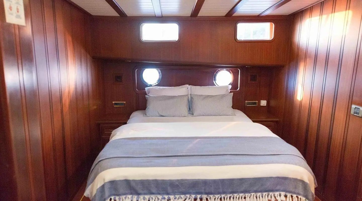 Primadonna yacht sleep area with bed, wooden cabin, striped bedding, porthole window