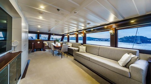 Virtuoso yacht interior with expansive windows, beige lounges, and a dining area on a sunny day