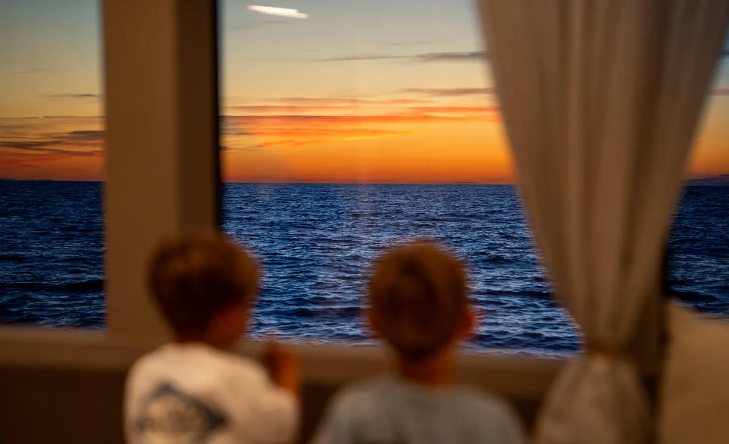 Two people watch a sunset over a calm sea from inside a yacht cabin, Nocturno