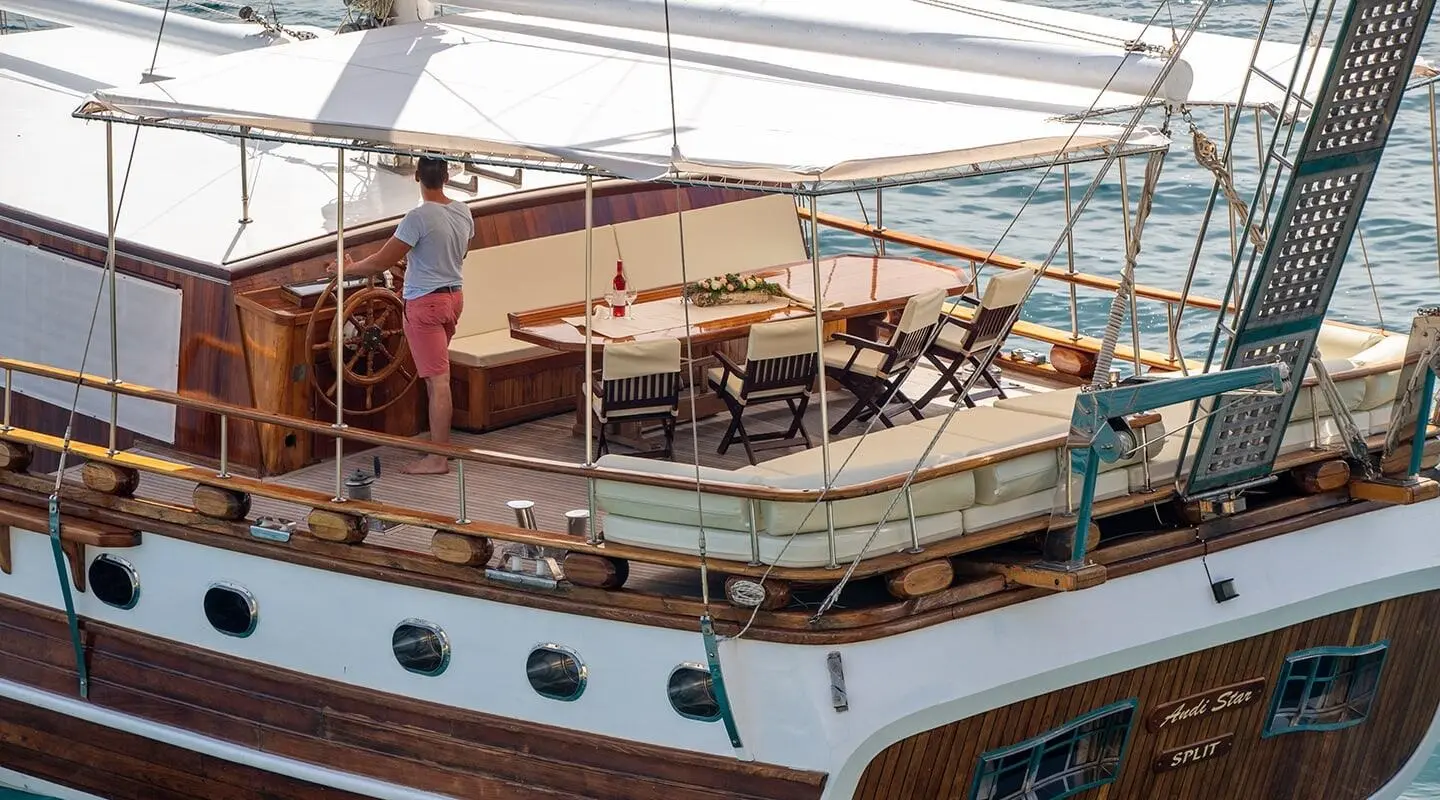 Andi Star yacht: teak deck, seating area, sails raised, calm water backdrop