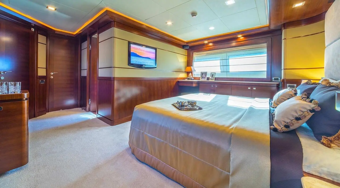 Luxurious bedroom on Seventh Sense yacht, polished wood accents and bed with beige linens
