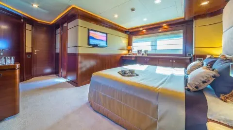 Luxurious bedroom on Seventh Sense yacht, polished wood accents and bed with beige linens