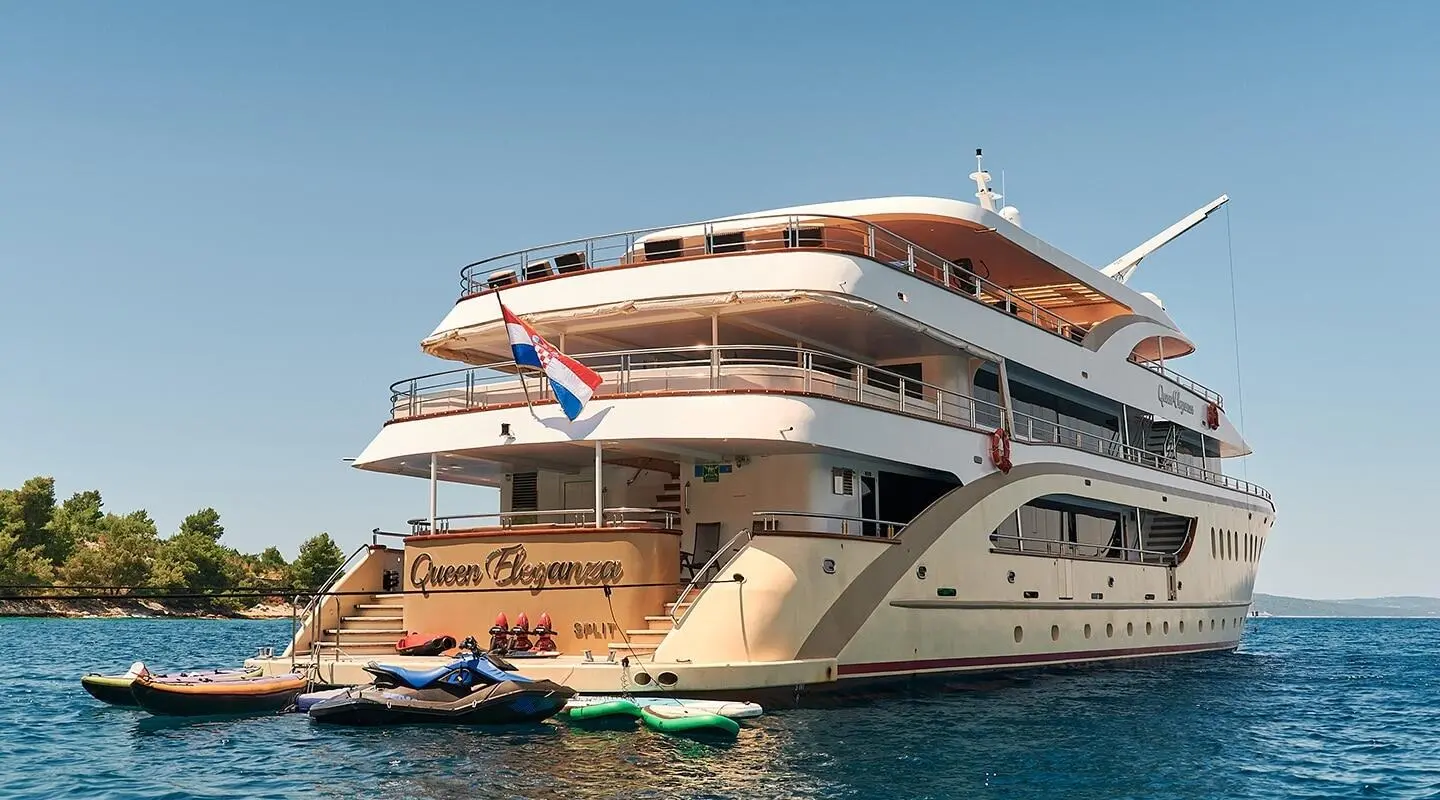 Queen Eleganza yacht anchored with people on deck and water sports boats