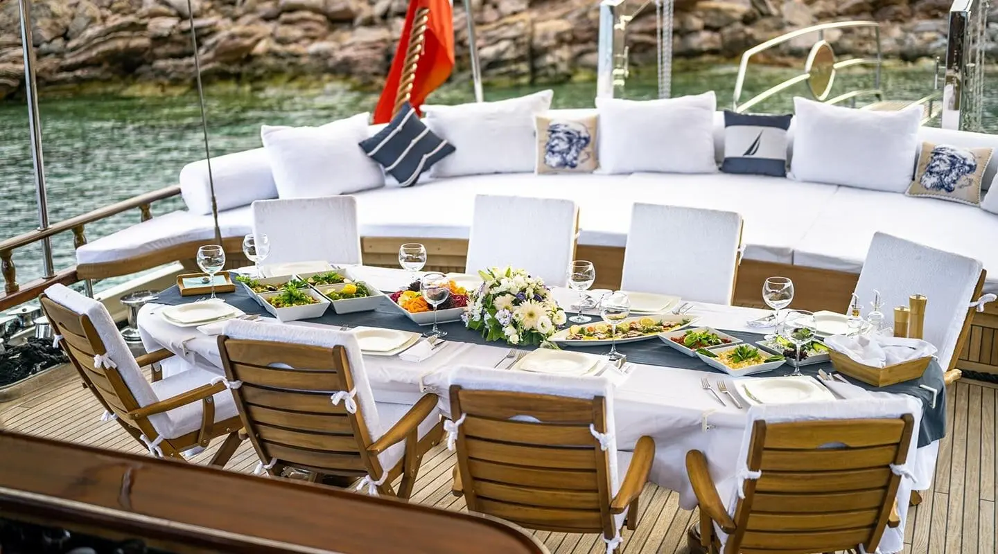 Estrella De Mar yacht deck laid out with white chairs and a long dining table at sunset