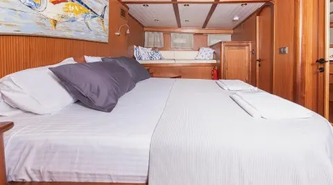 Interior of Bodrum Queen yacht with large bed, wooden cabinets, and porthole
