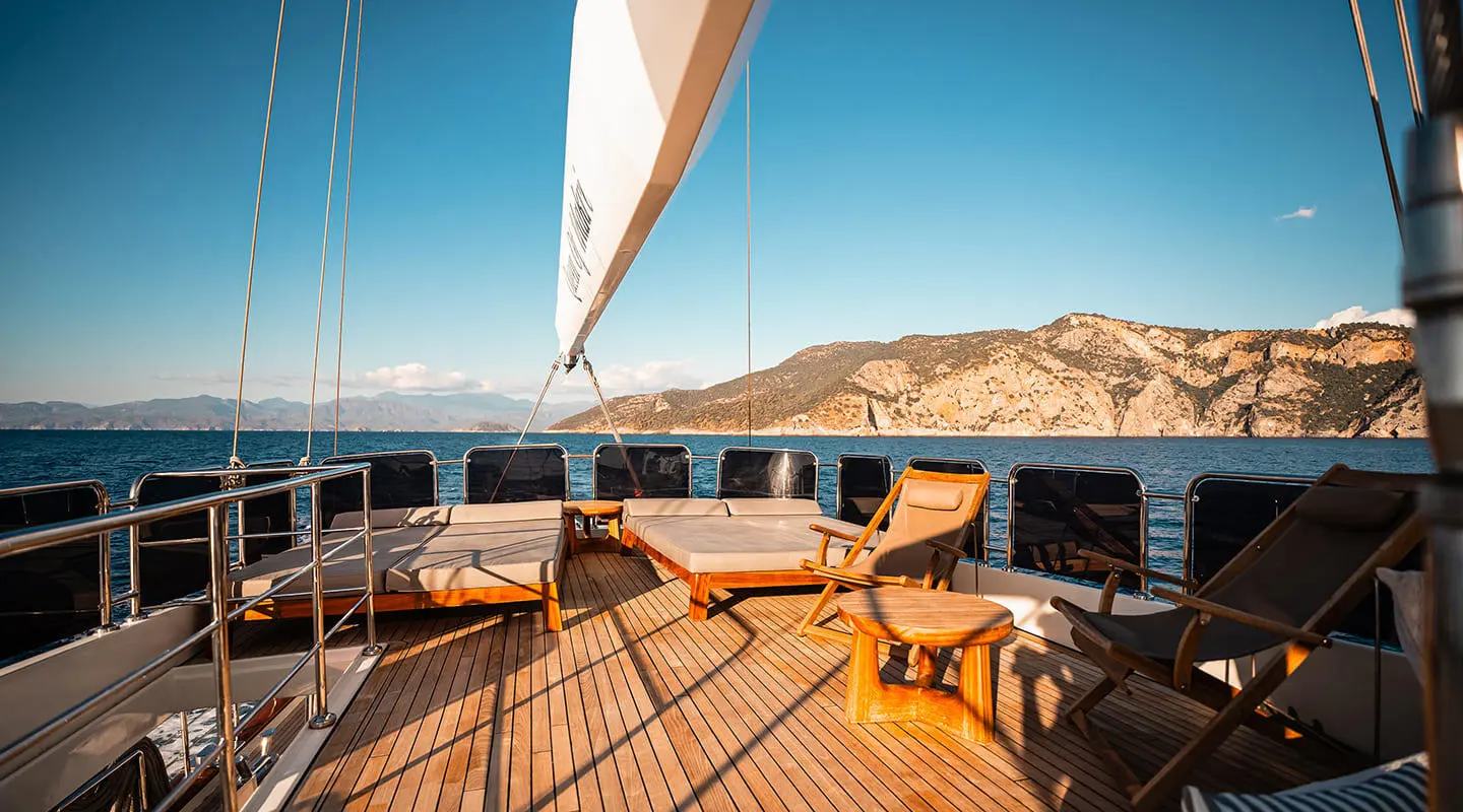 Top deck of Queen Of Makri gulet with sails and coastline in background