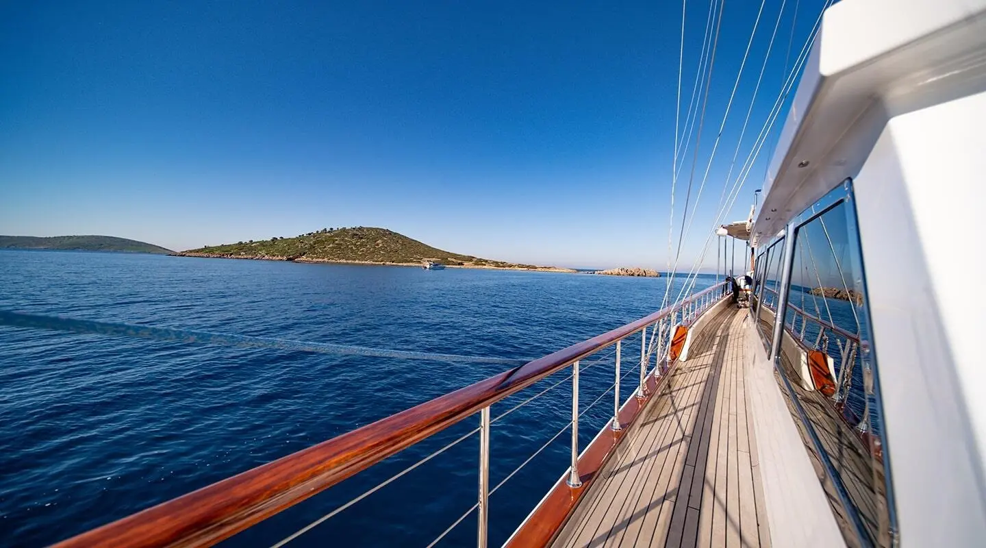 Sailing yacht Double Eagle deck with railing, calm sea, island horizon at sunset