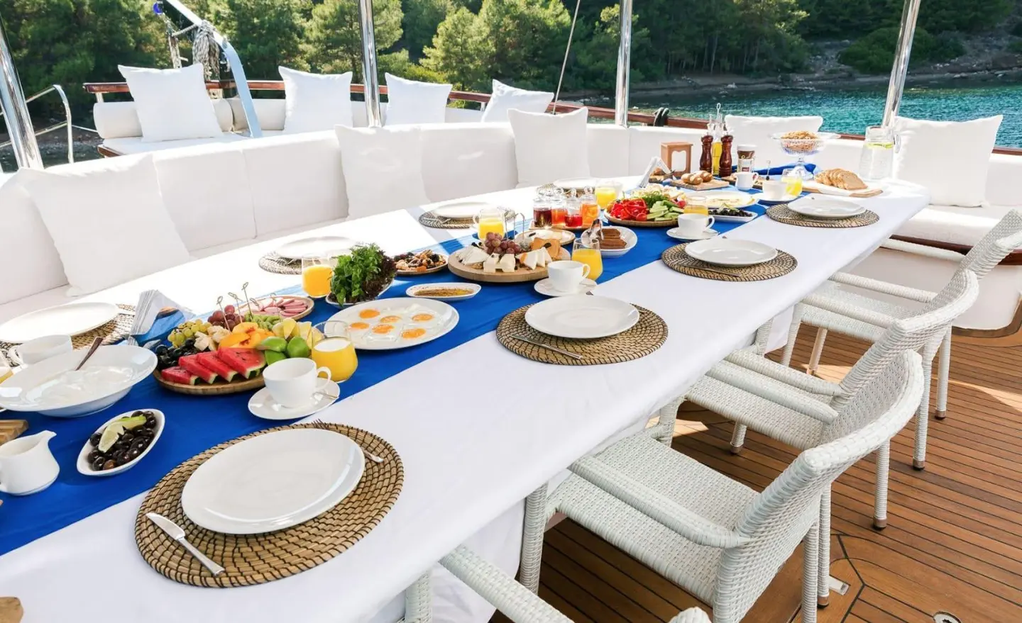 Halcon Del Mar yacht with a long dining table setup on deck at sunset