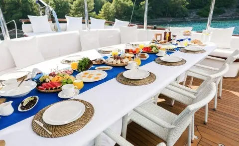 Halcon Del Mar yacht with a long dining table setup on deck at sunset