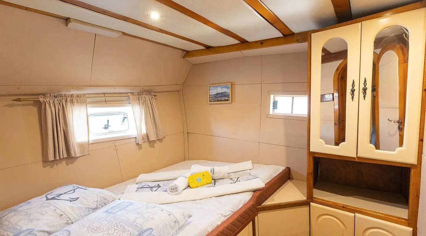 Interior cabin with a bed, porthole windows, and wooden cabinets