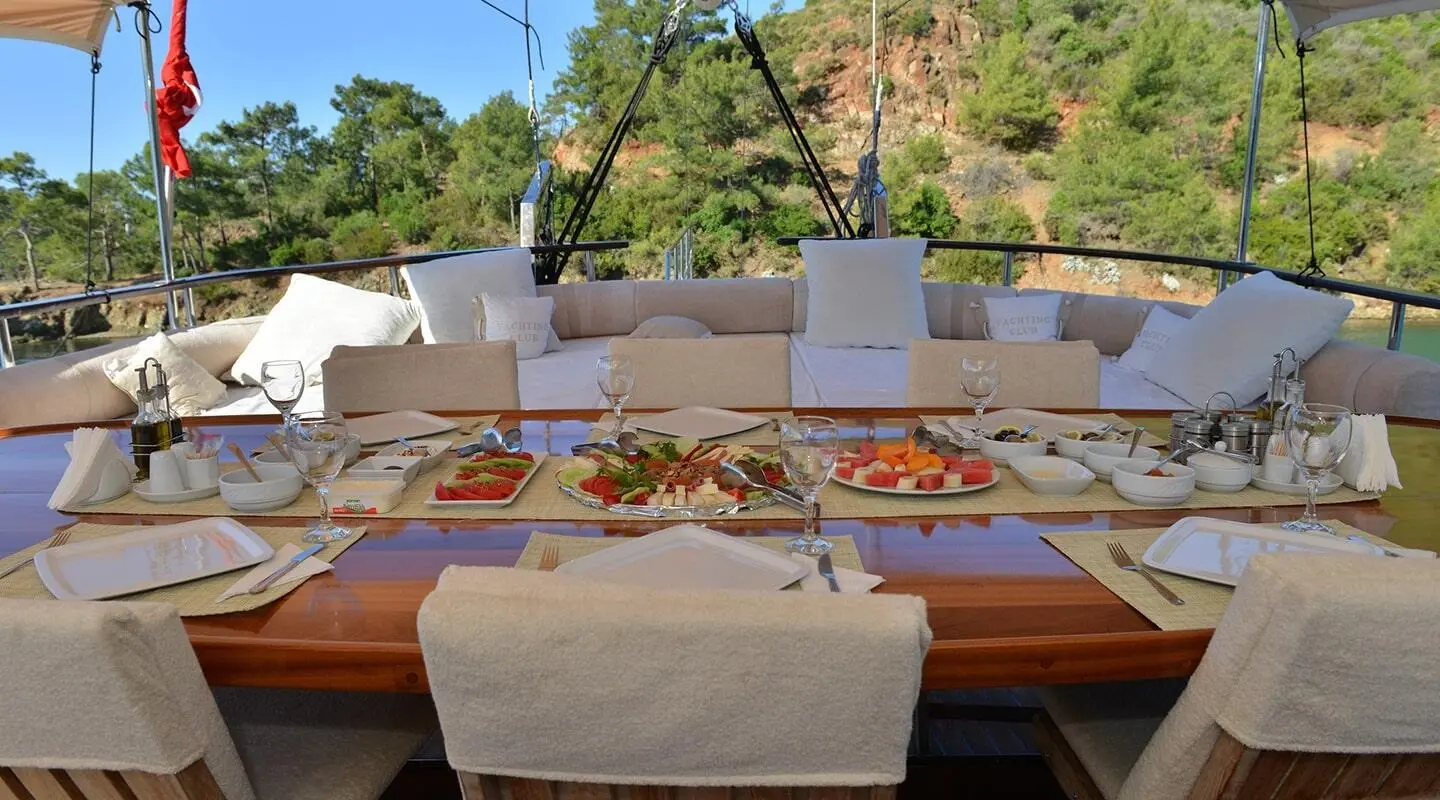 Derin Deniz yacht with a dining table set on deck at sunset, soft cushions and palm trees