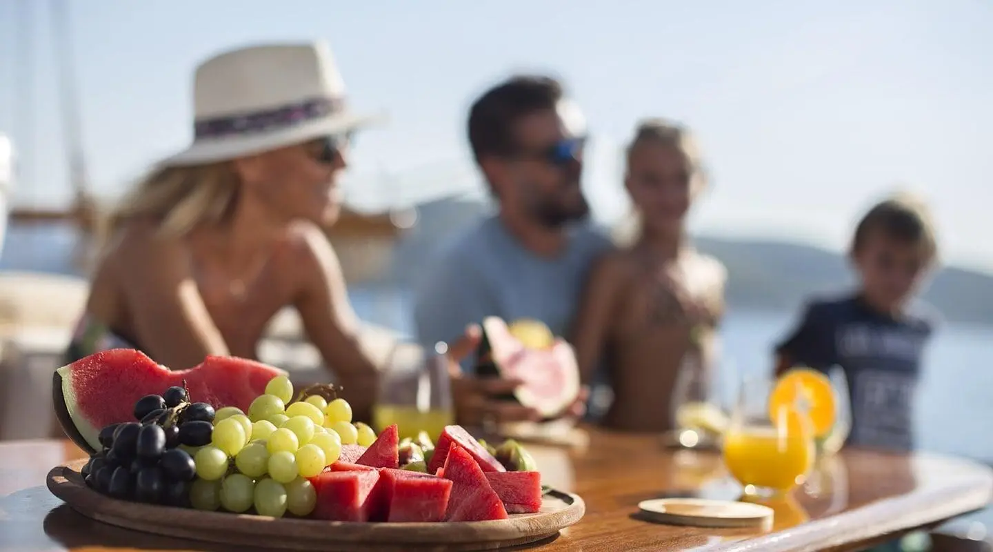 Entre Cielos yacht on a sunny deck with fresh fruit platter and guests enjoying the breeze