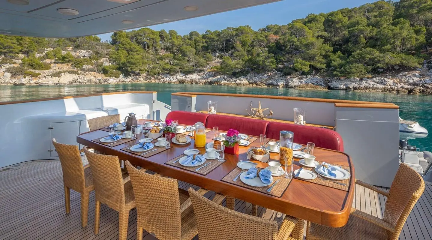 Gularos yacht dining area with a long wooden table set for meals on deck at sunset