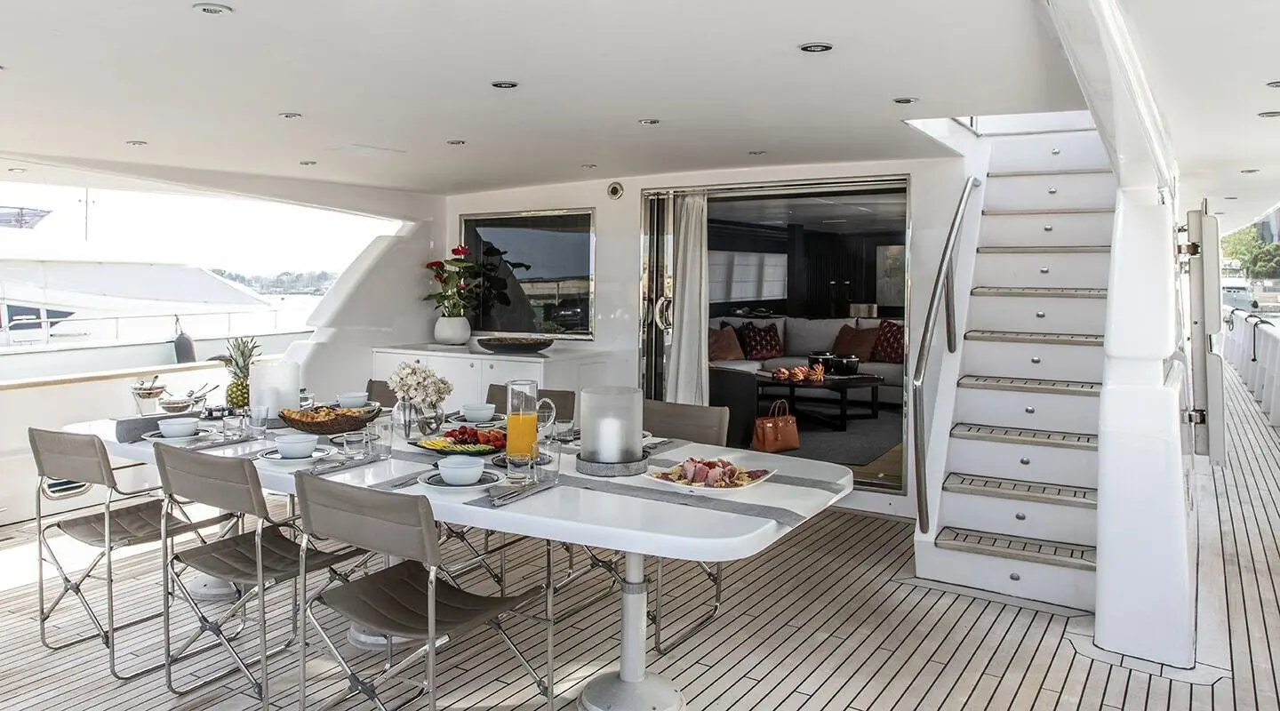 Wide teak deck dining area on yacht with tables, chairs, and built-in seating
