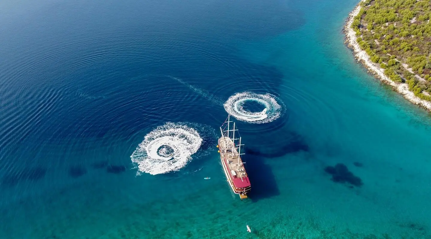Top-down view of a white luxury sailboat near a red-hulled yacht anchored in clear blue water