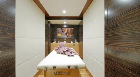 Meira yacht massage room with a bed, towels, and warm wood accents.