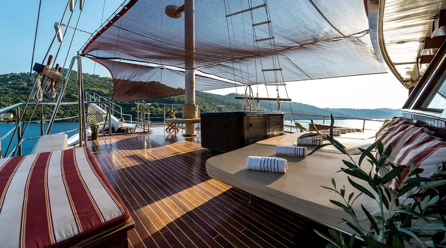 Cesarica yacht deck with wooden stairs, seating, and rigging at sunset harbor