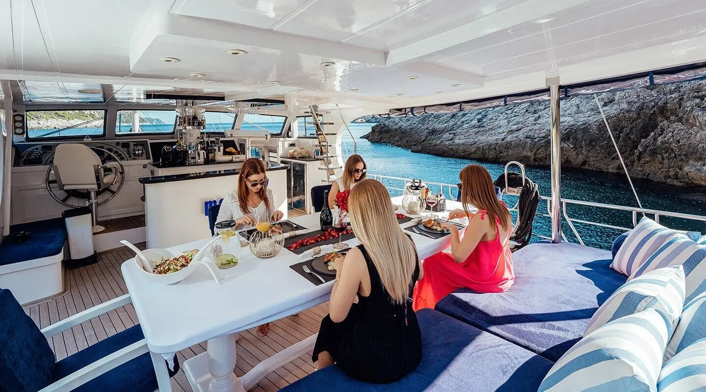 Maske yacht dining on deck with guests at a long table by the sea