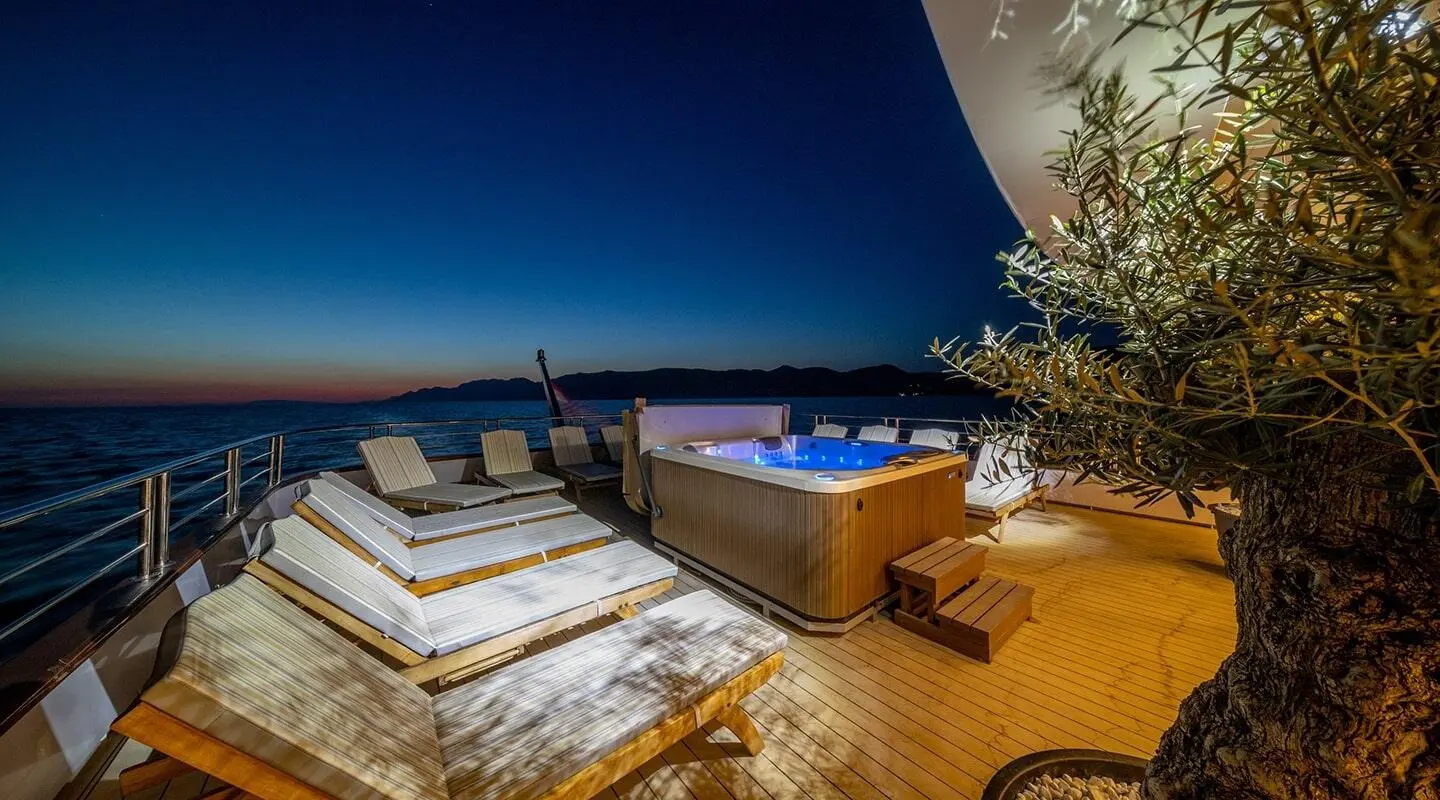 Open deck of a yacht at sunset with a hot tub and lounge chairs on the teak deck