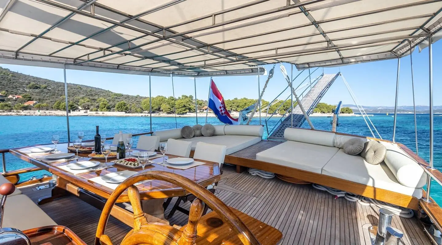 Andi Star yacht deck at sunset with helm wheel and seating under canopy