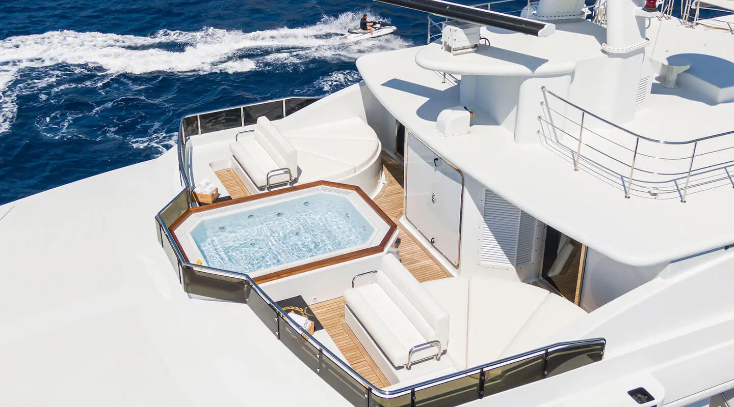 A luxury yacht Apogee deck with a hot tub, white seating, and blue water