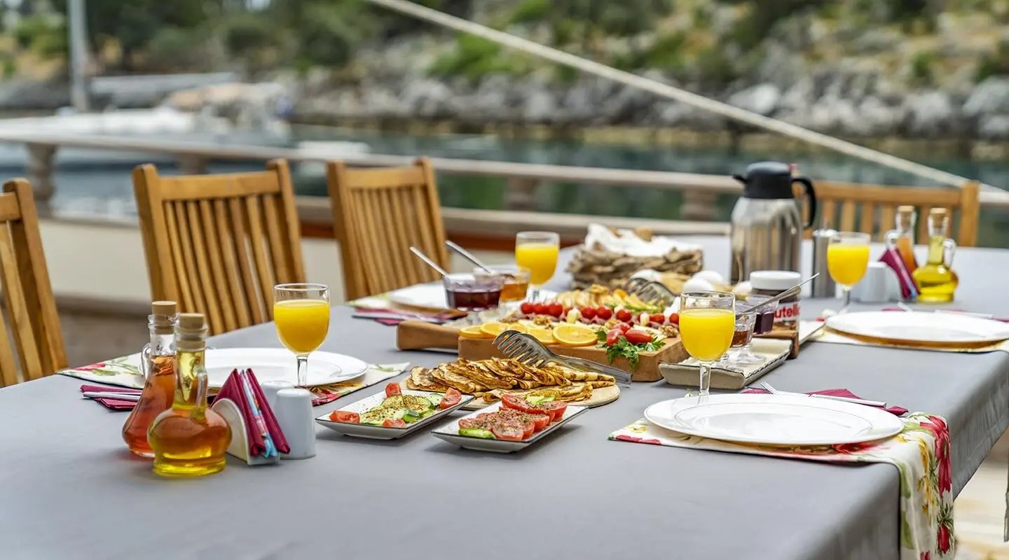 Tersane 8 yacht dining setup with plates, fruit, and beverages on deck at sunset