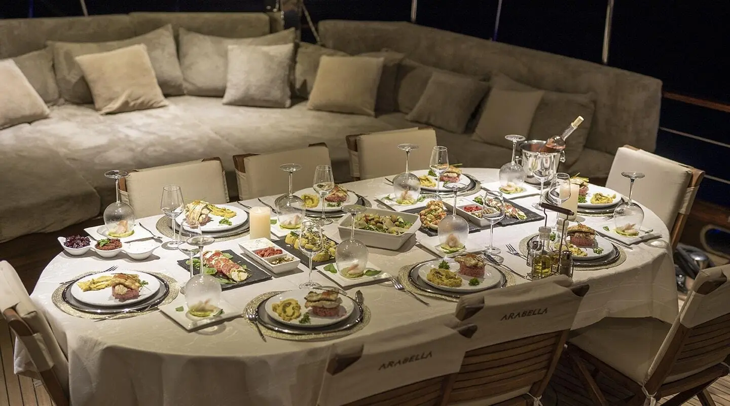 Arabella yacht dining on deck with a luxurious table setting and plush lounge backdrop