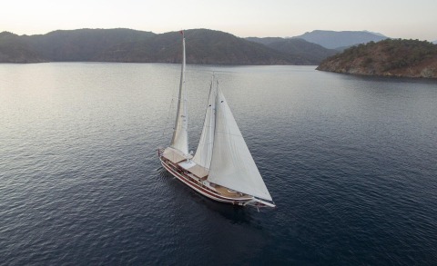Two-masted gulet sailing yacht on the sea with rocky hills in the background