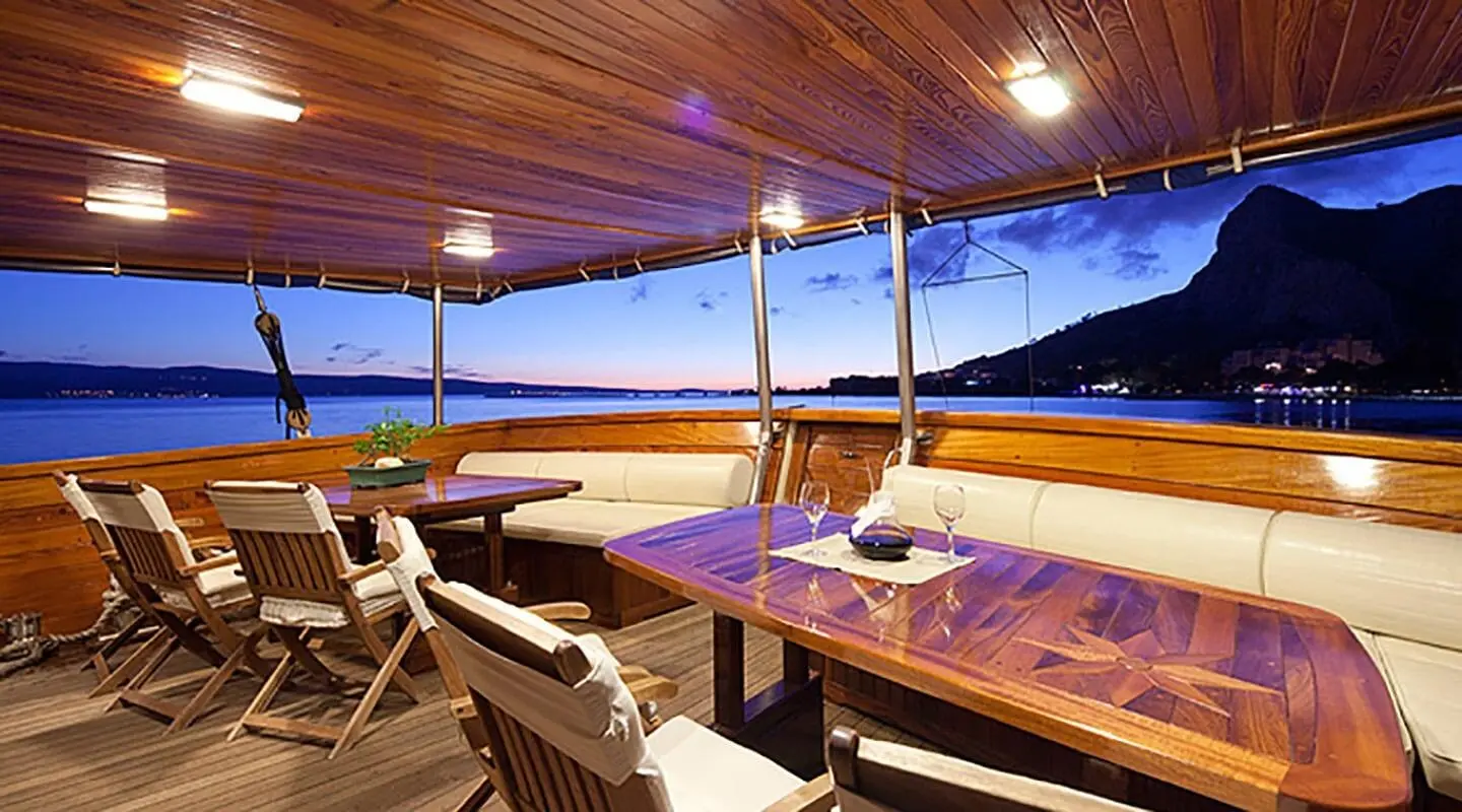 A aft deck of Tajna Mora yacht with wooden seating, sun loungers, and string lights
